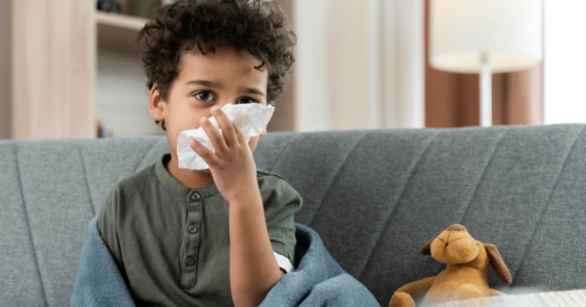 little boy sick looking sick sitting on the couch blowing his nose